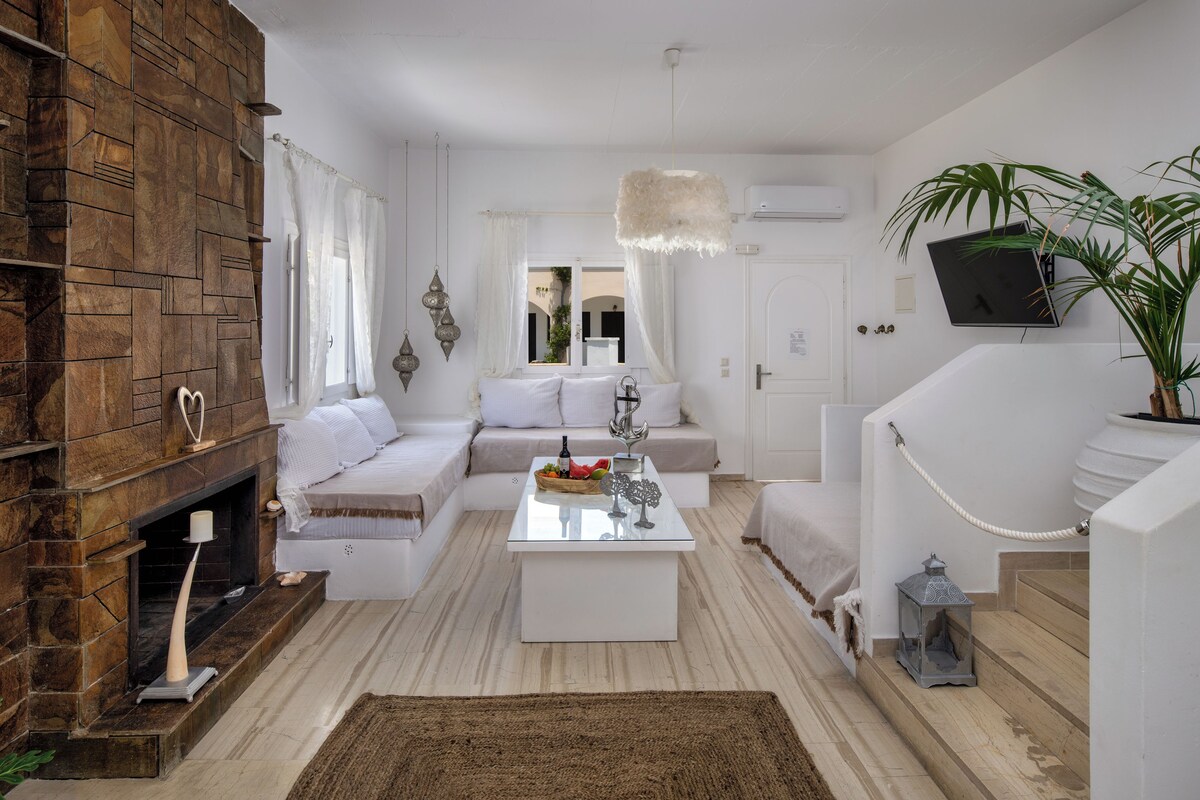 A modern living room with a stone fireplace, white sofas, a glass coffee table, and a potted plant.