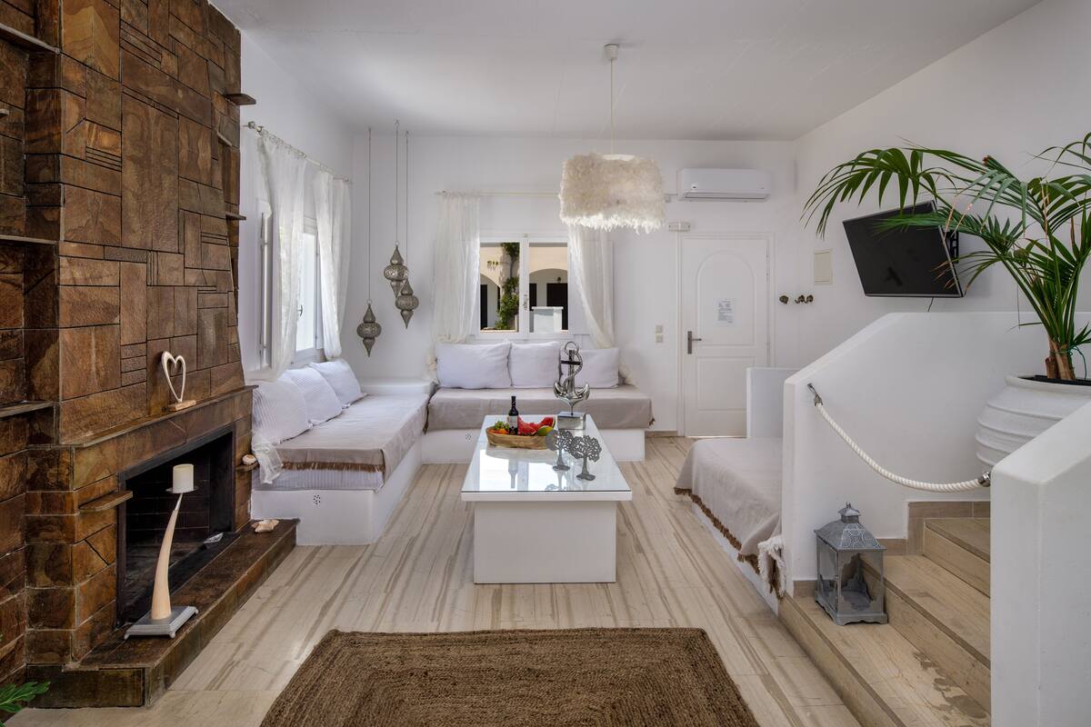 A modern living room with a stone fireplace, white sofas, a glass coffee table, and a potted plant.