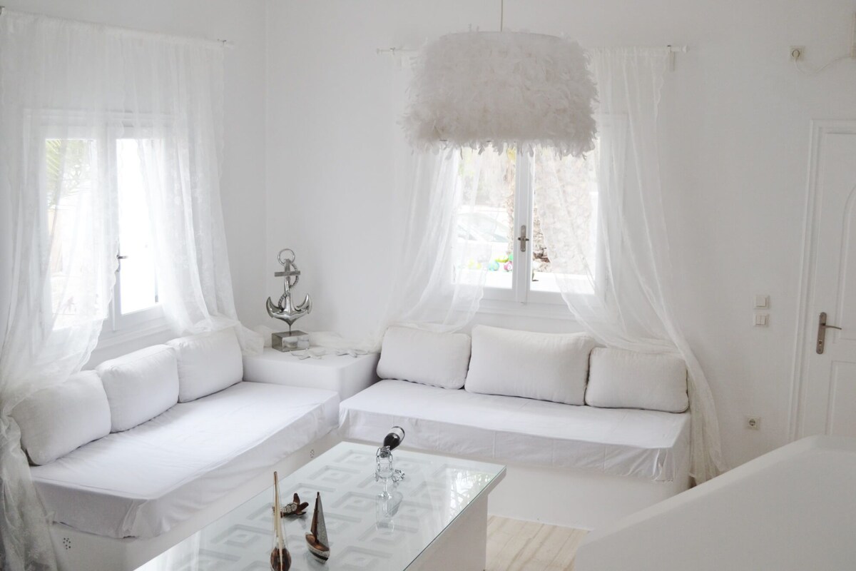 Een witte kamer met een bank, een glazen salontafel en een decoratief anker.