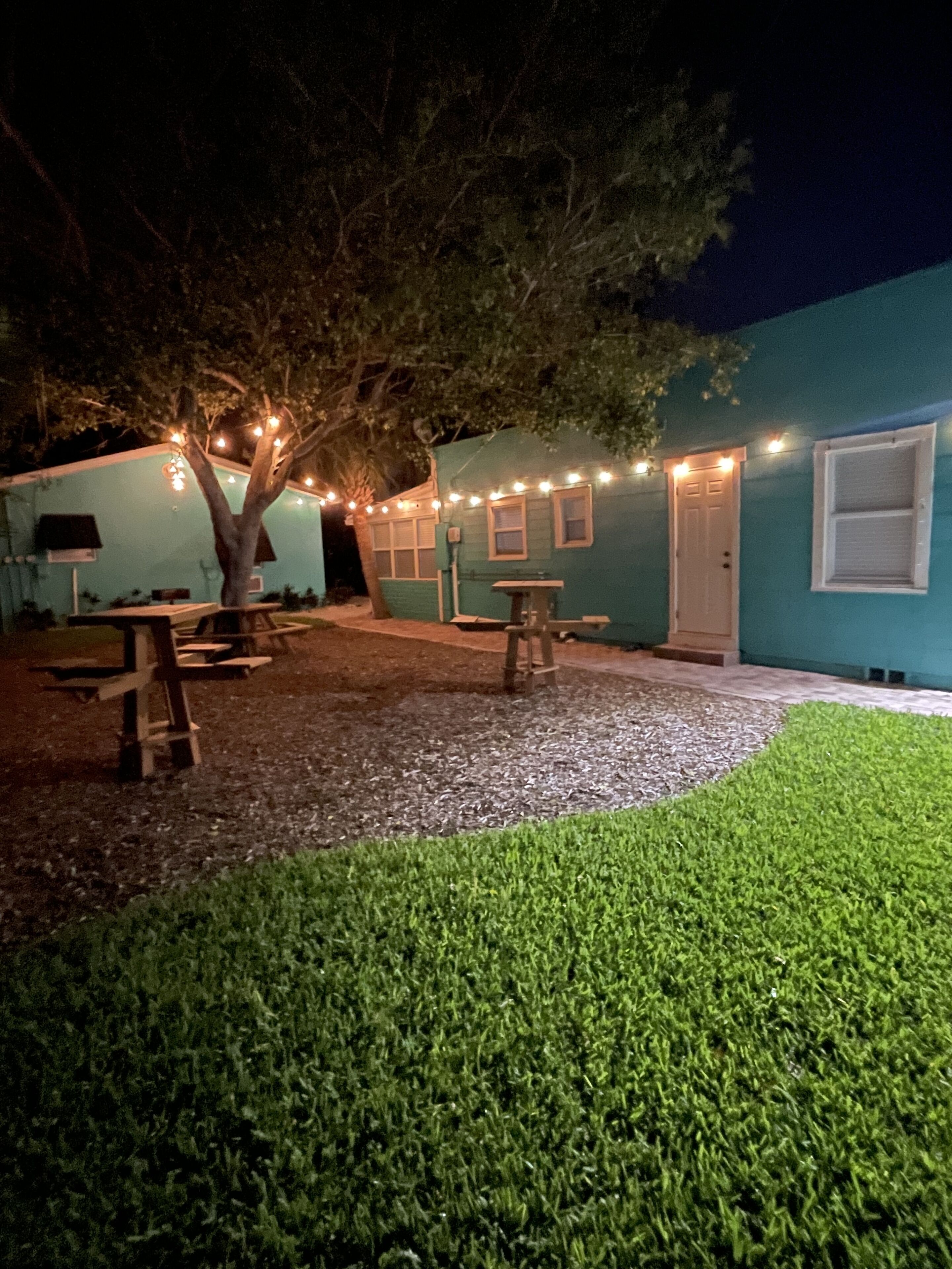 A patio area with a tree, picnic tables, and string lights.