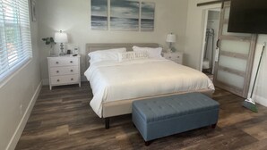 Un dormitorio con una cama grande, mesitas de noche, un banco y obras de arte en la pared.