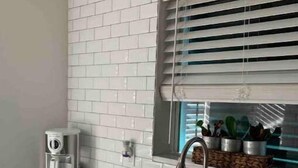 Una cocina con baldosas blancas tipo metro, un lavamanos de acero inoxidable y una ventana con persianas.