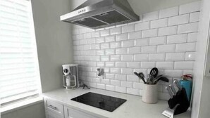 Una cocina con armarios blancos, un lavamanos negro y una campana extractora de acero inoxidable.