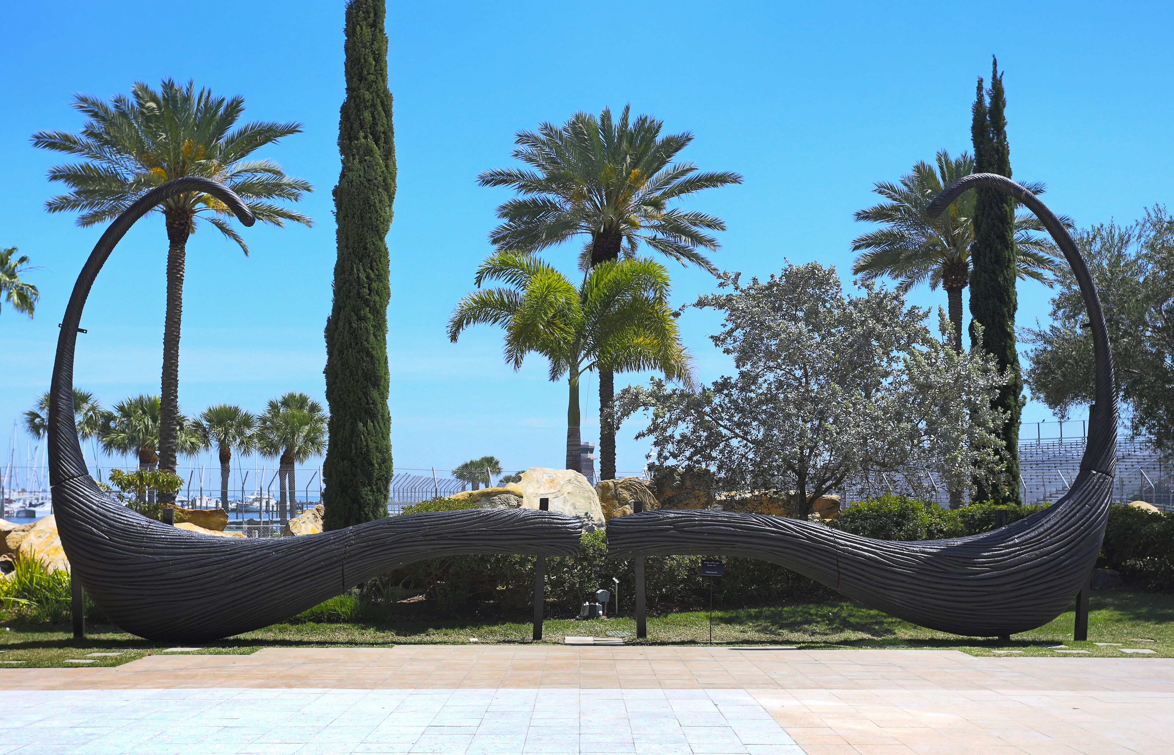 A hammock sculpture in a park with palm trees and a clear sky.