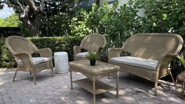 Un espacio de descanso al aire libre con muebles de mimbre, dos sillones y una mesita, rodeado de follaje.