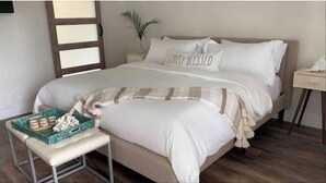 Un dormitorio ordenado con cama, mesitas de noche y un pequeño banco.