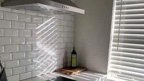 Una cocina con armarios blancos, estufa negra y ventana con persianas.