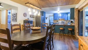 Ein Holzesstisch mit Stühlen, eine Küchenzeile mit blauen Schränken und eine Bar mit Hockern.