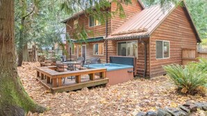 Eine Holzhütte mit Whirlpool, Terrasse und Sitzbereich im Freien, umgeben von Bäumen.