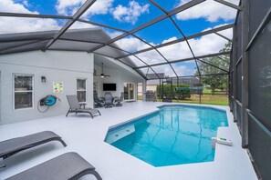 A covered outdoor swimming pool with lounge chairs, a ceiling fan, and a view of the backyard. - House with backyard on the golf course, Park Place (Haines City)