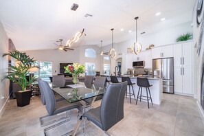 A modern kitchen with white cabinets, stainless steel appliances, and a glass dining table with black chairs. - House with backyard on the golf course, Park Place (Haines City)