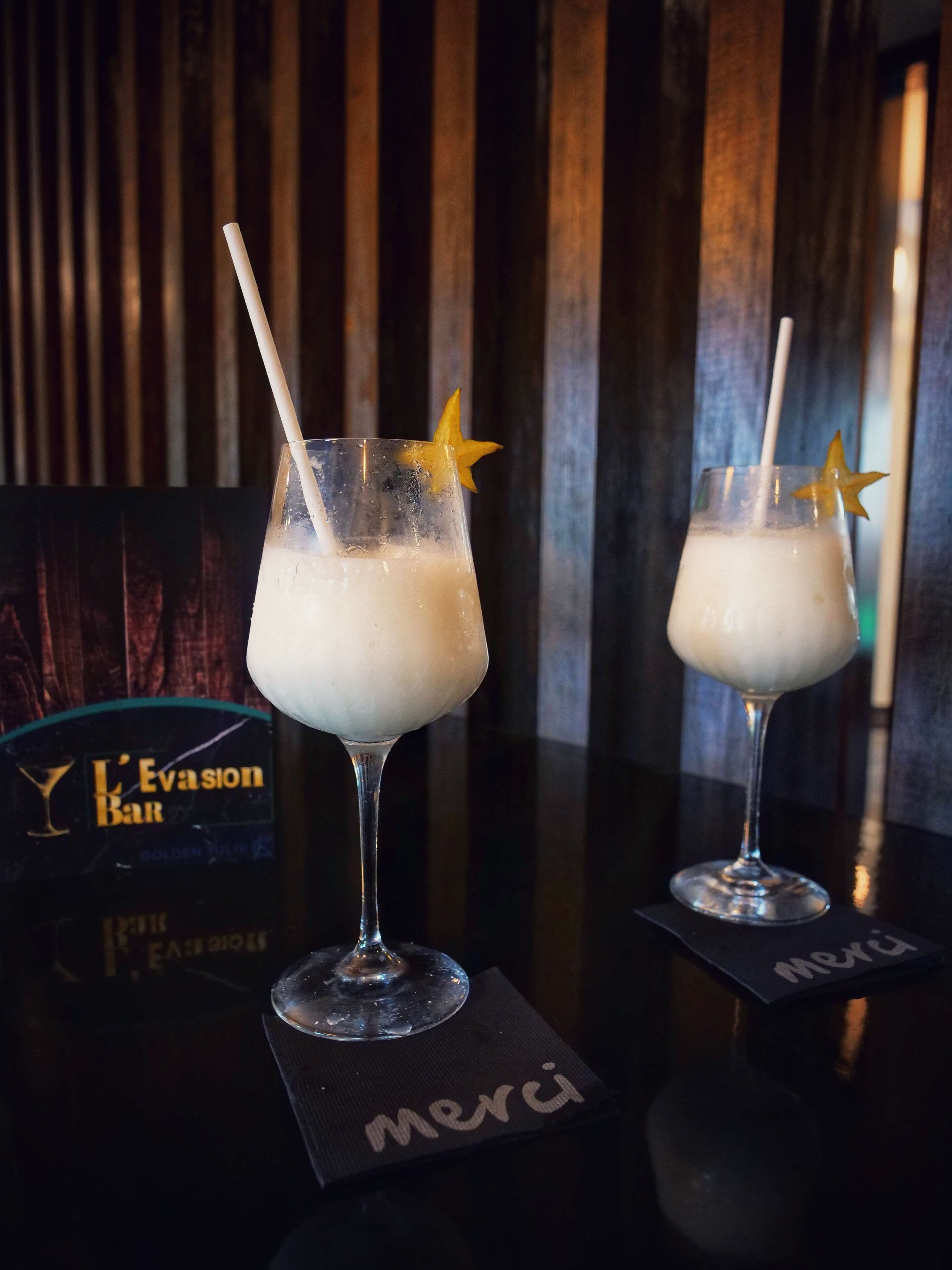 Two glasses of a creamy beverage with star-shaped garnishes on a bar counter, with a 'L'Evasion Bar' sign in the background.