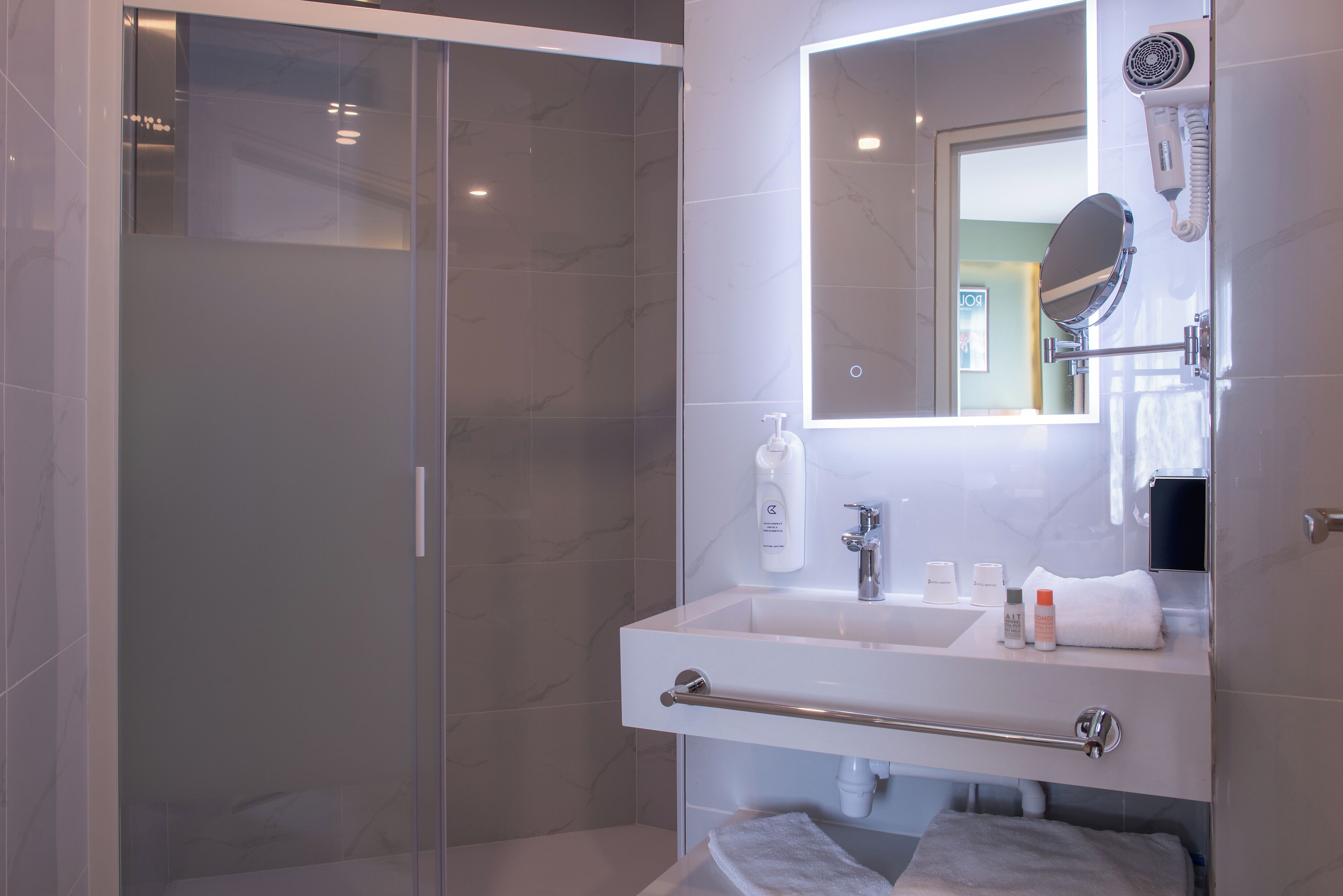 Un baño moderno con ducha envuelta en vidrio, un espejo grande y tocador con toallero.