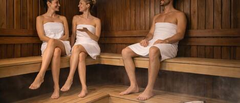 Tres personas sentadas en bancos de madera dentro de un sauna con suelo de piedra.