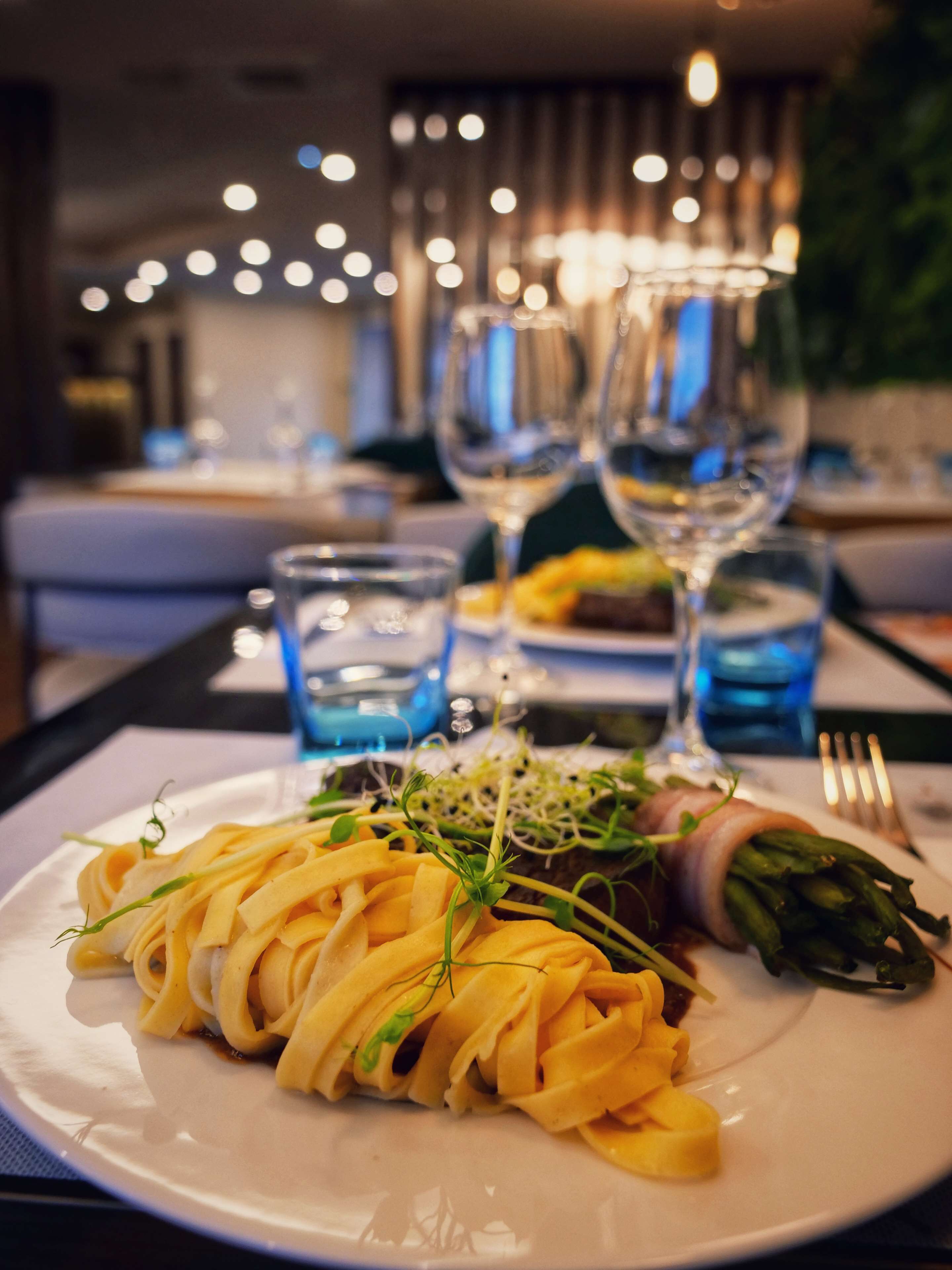 A dining table with a plate of pasta, asparagus, and a glass of water.