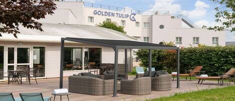 A covered outdoor seating area with wicker furniture and a glass-enclosed room with chairs and tables.
