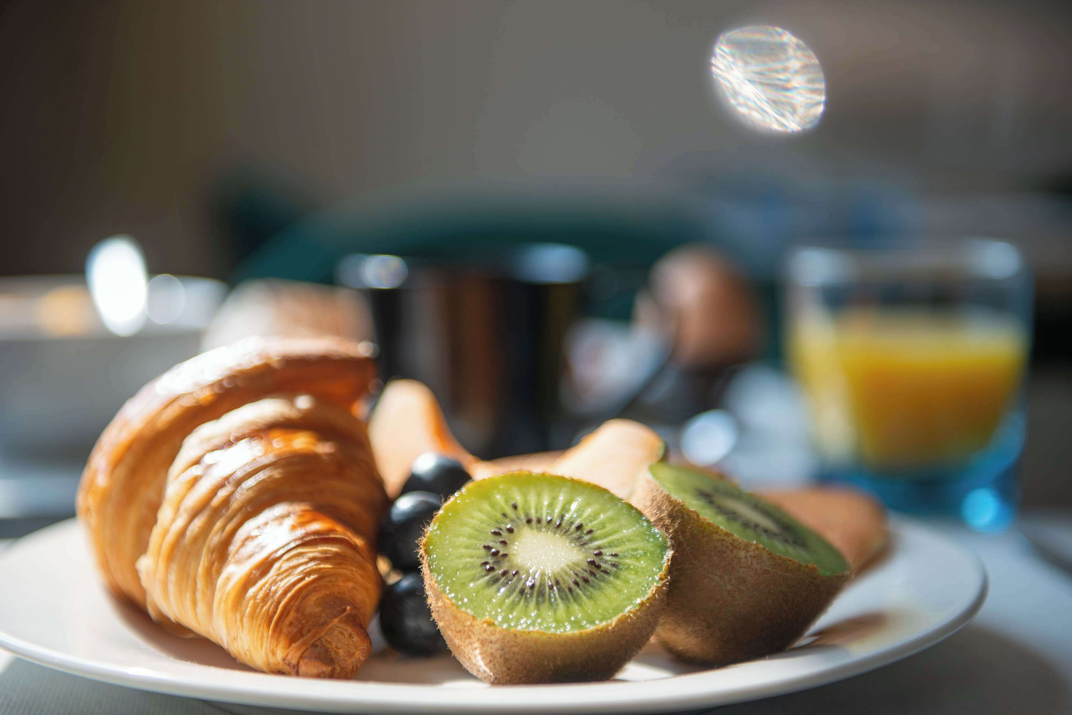 A plate with a croissant, kiwi slices, and grapes.