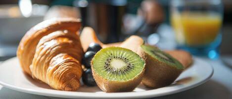 A plate with a croissant, kiwi slices, and grapes.