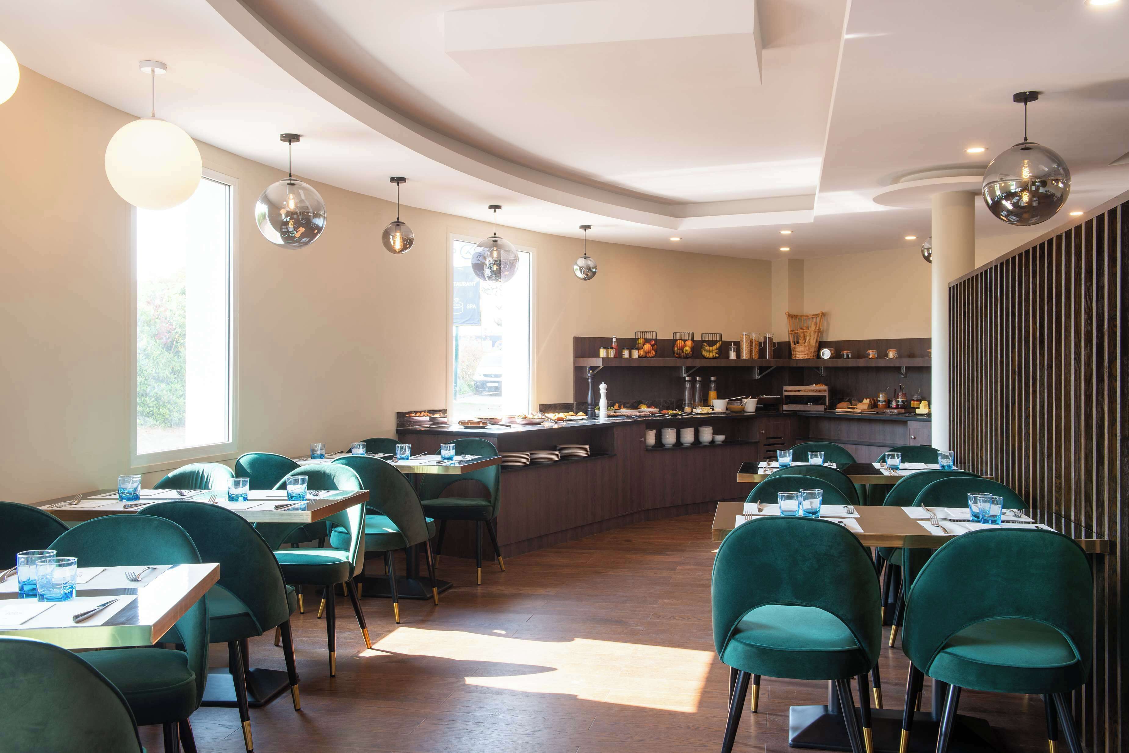 Un espace de restauration moderne avec des chaises à revêtement vert, des tables en bois et des luminaires suspendus.