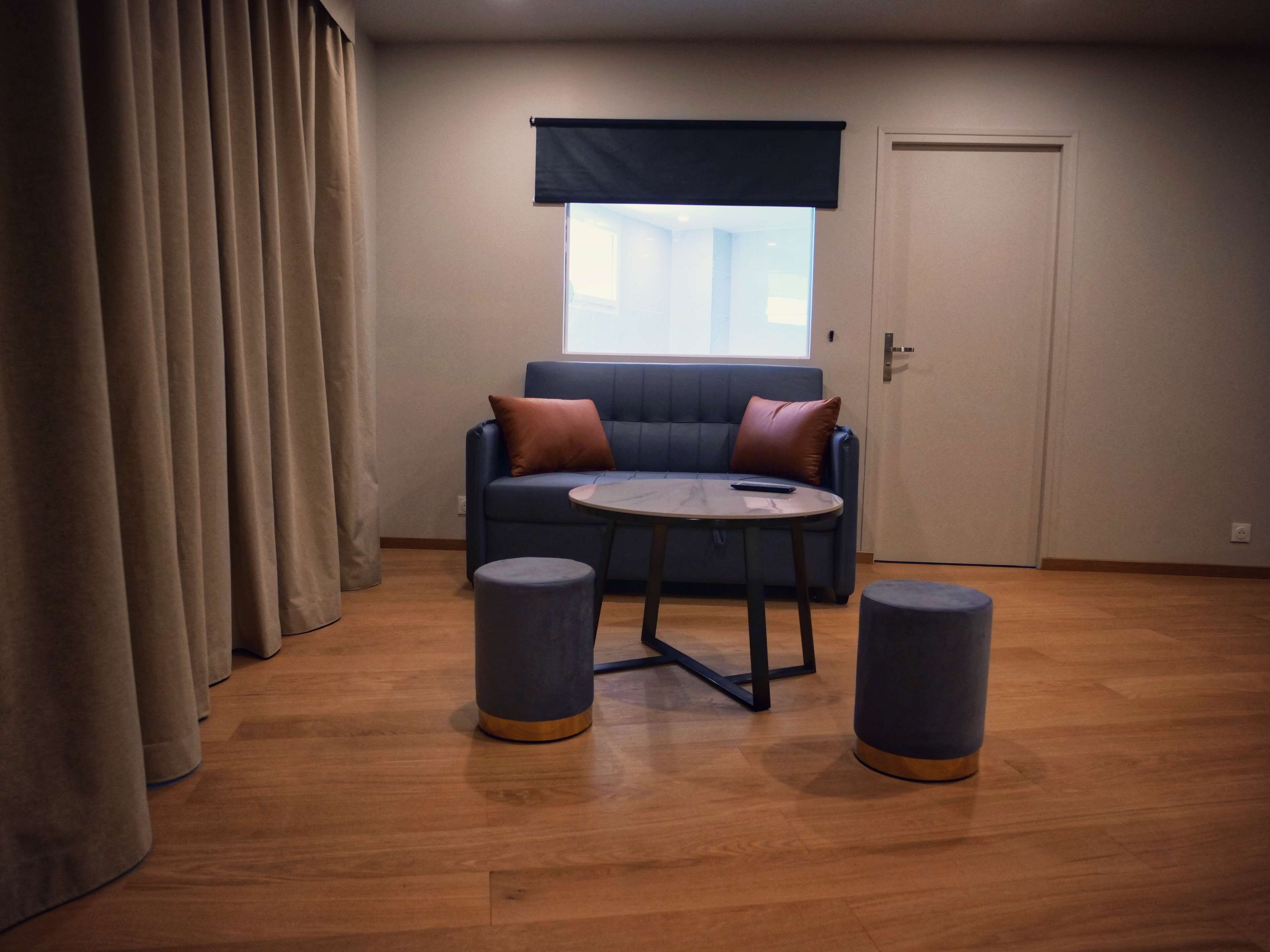 Una sala de estar moderna con un sofá azul, dos otomanas redondas, una mesita y un ventanal con vistas.