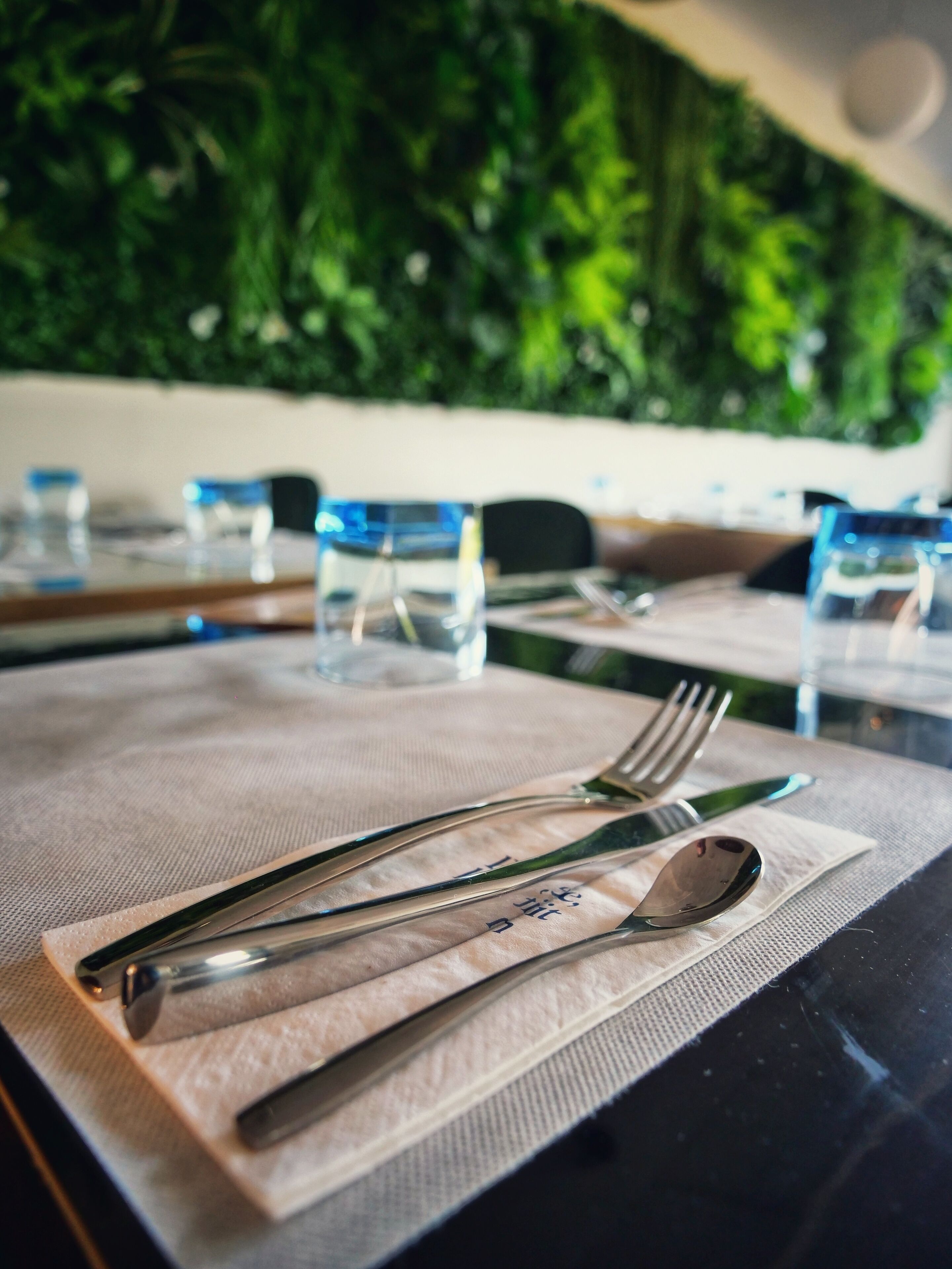 Una mesa dispuesta con cubiertos y copas, con una pared verde al fondo.