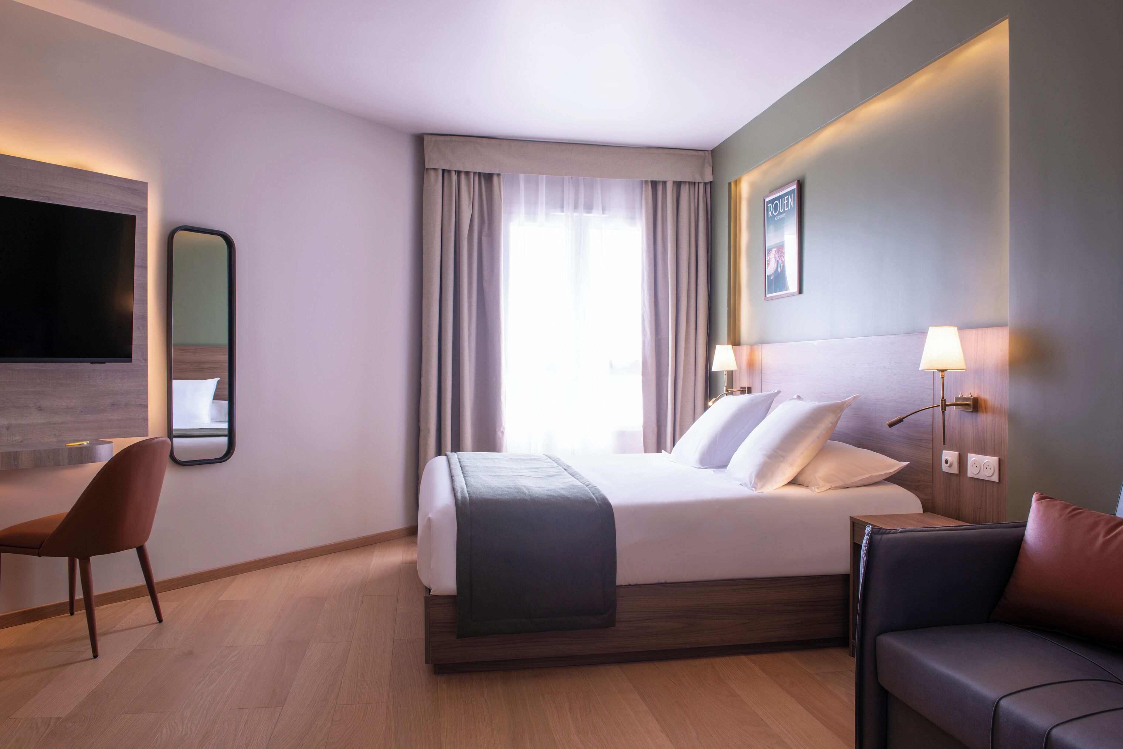 Moderni hotellihuone, jossa on sänky, työpöytä, tuoli ja televisio.
