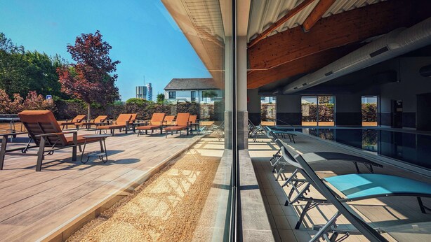 Un espace extérieur aménagé, abrité et doté de fauteuils confortables et d’une table de billard, offrant une vue sur un jardin paysager et un bâtiment situé au loin.