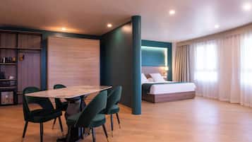 Een moderne hotelkamer met een zithoek, een bed met hoofdeinde en een groot raam met gordijnen.