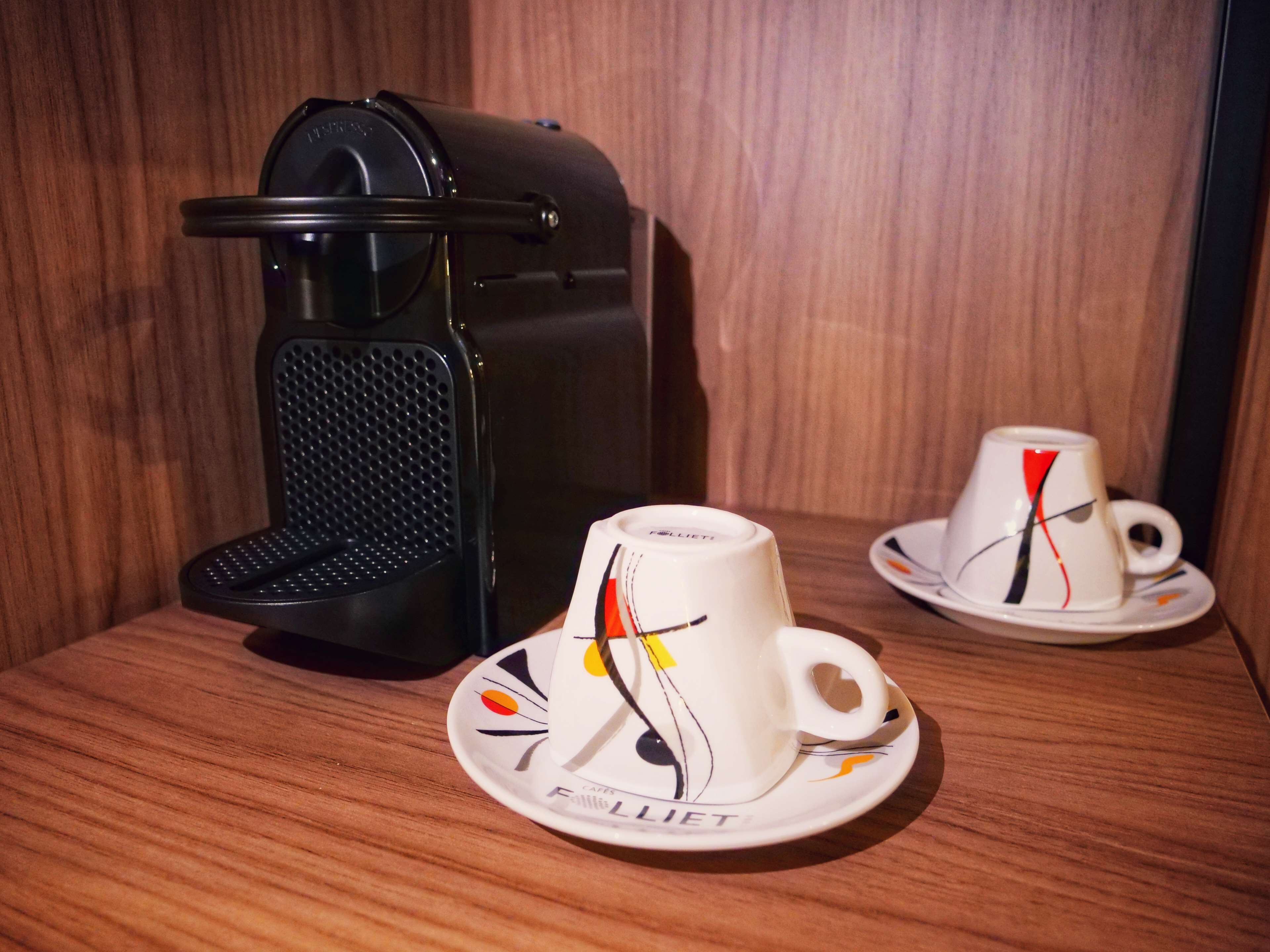 Una máquina de café y dos tazas con un diseño de nota musical sobre una superficie de madera.