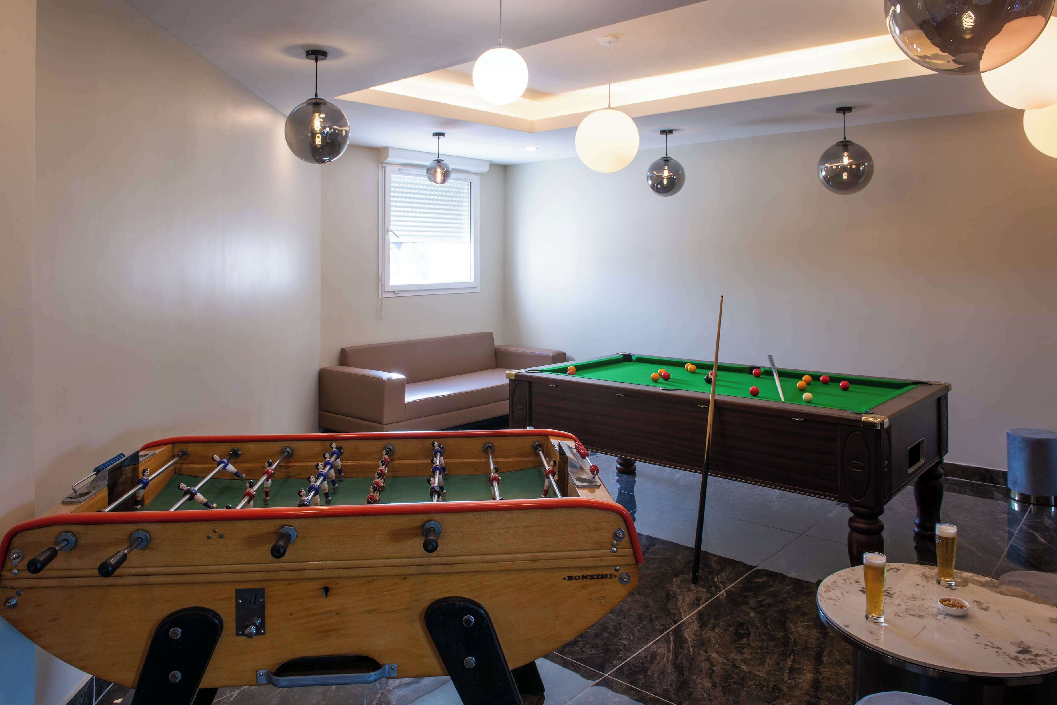 Ein Raum mit Tischfußball, Billardtisch, einer Couch und einem kleinen runden Tisch mit zwei Biergläsern.