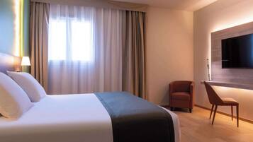 Een hotelkamer met een groot bed, een bureau, een stoel en een wandgemonteerde flatscreen televisie.