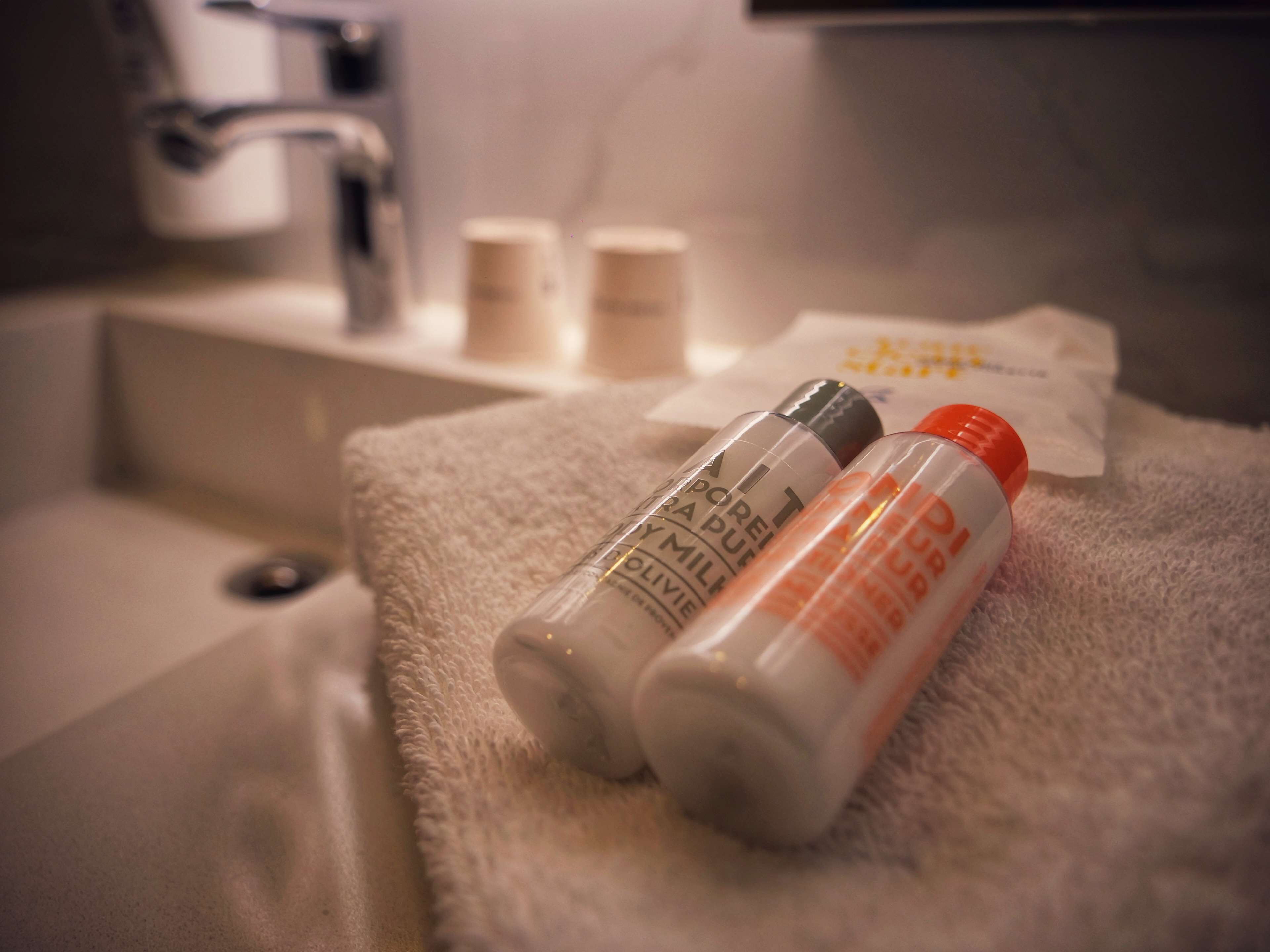 A bathroom with a white sink, two bottles of lotion, and a towel on a white bath mat.