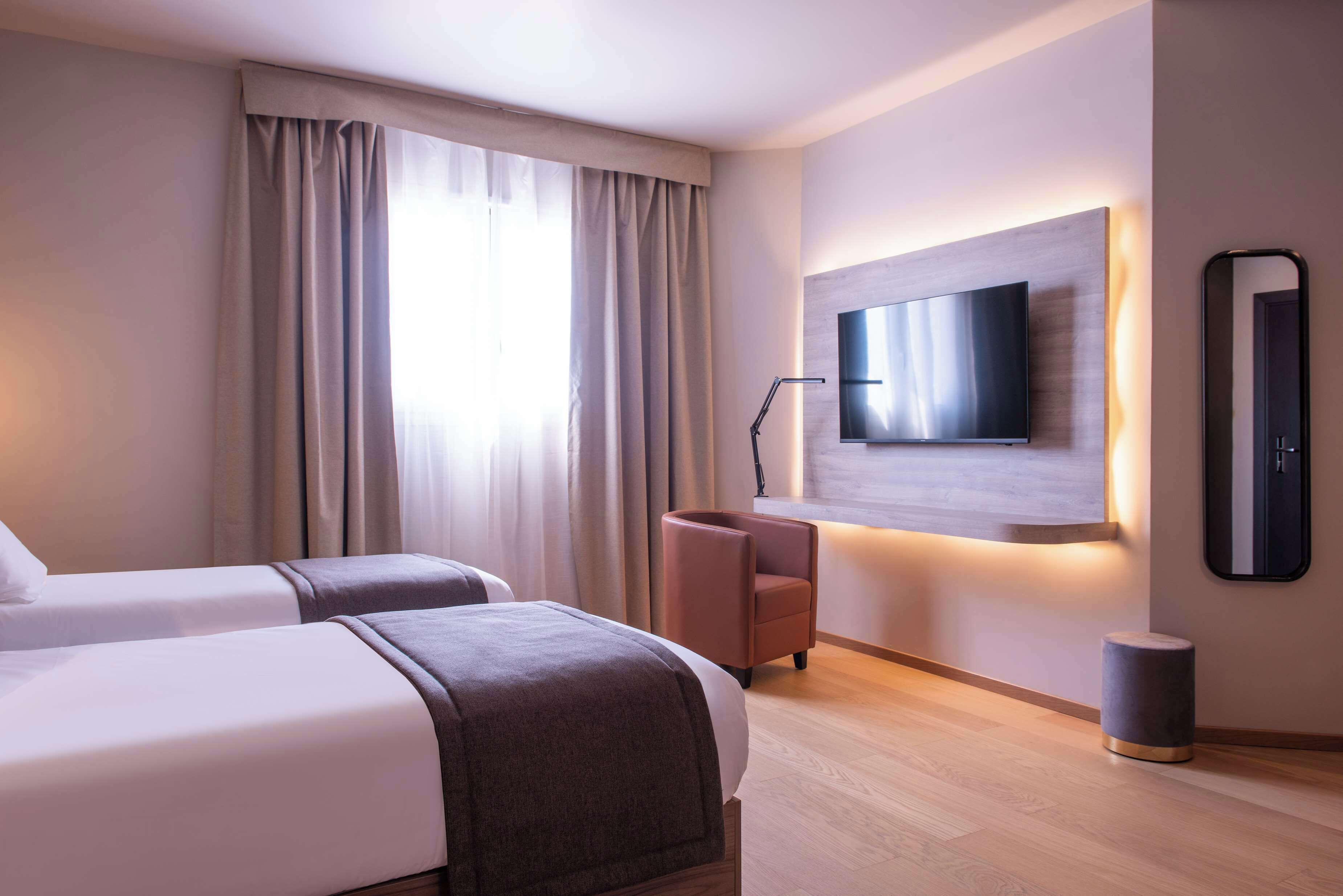 A hotel room with two beds, a TV mounted on the wall, a chair, and a small round table.