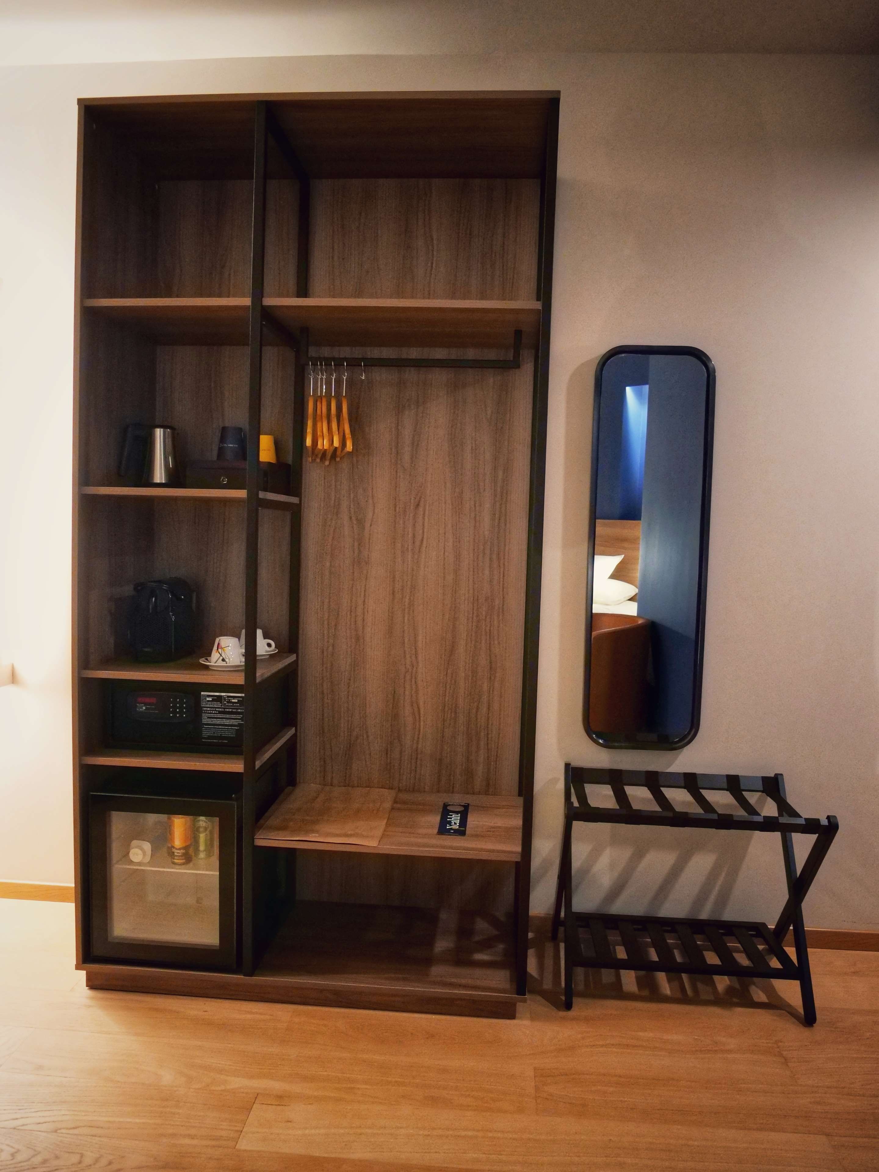 A wooden wardrobe with multiple shelves, a small table, and a mirror.