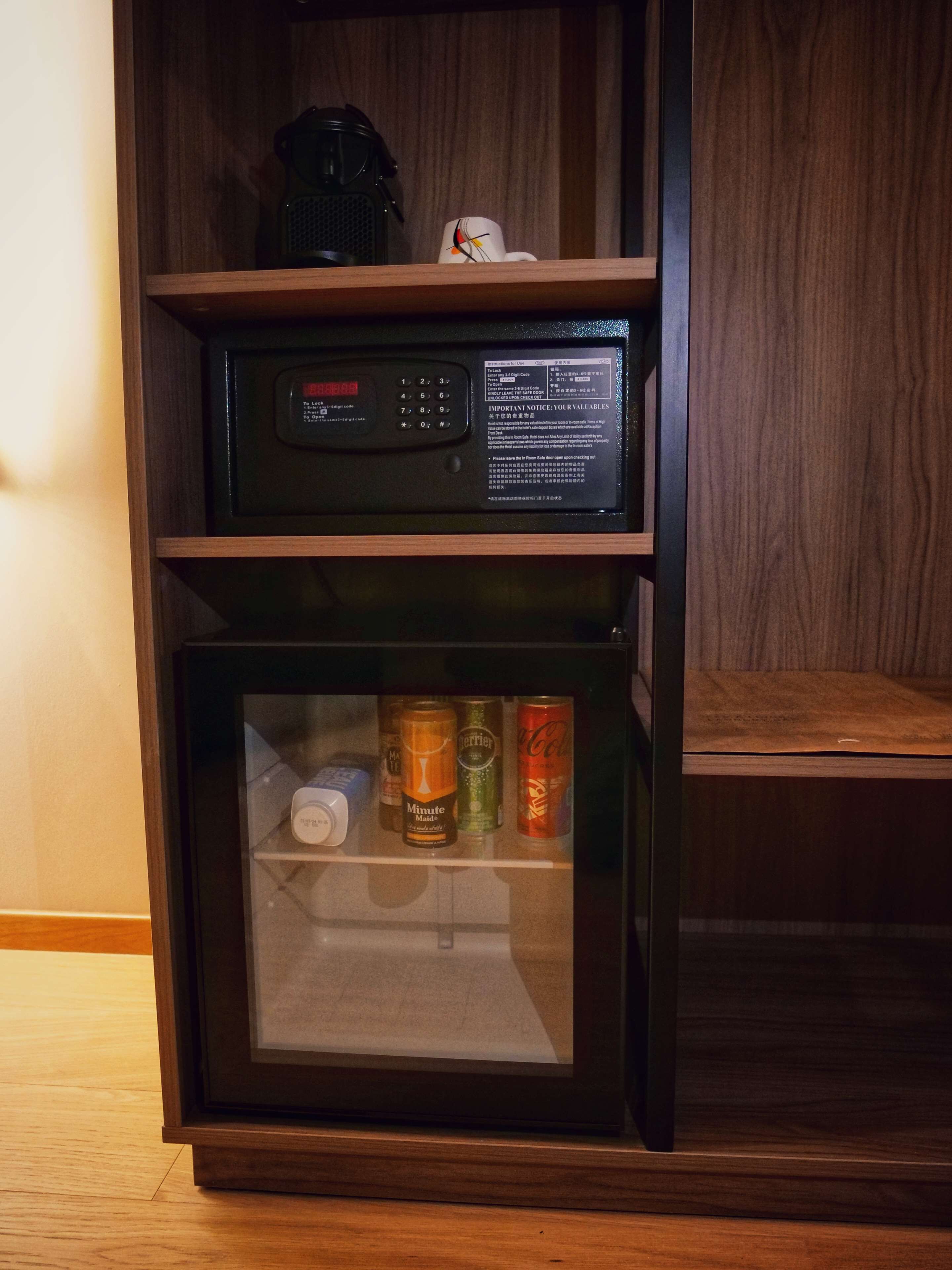 A minibar with a coffee maker, a small refrigerator containing beverages, and a digital display.