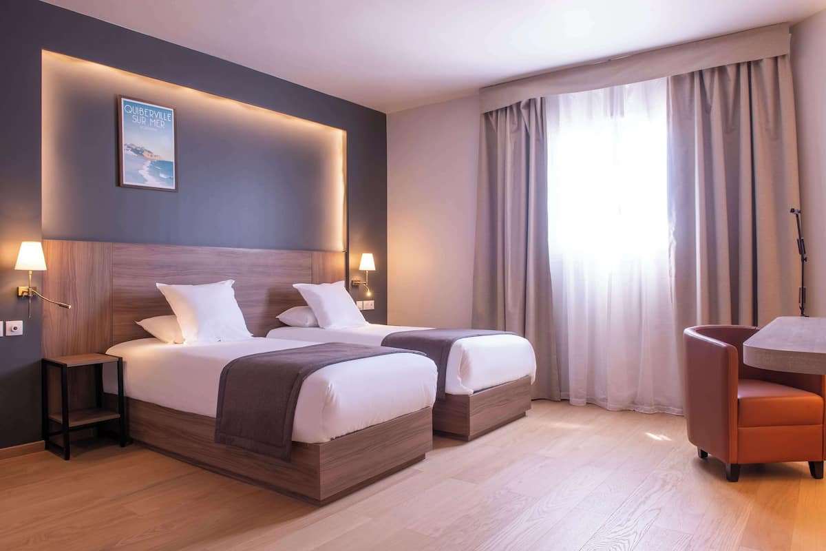 A hotel room with two beds, a desk, and a chair.
