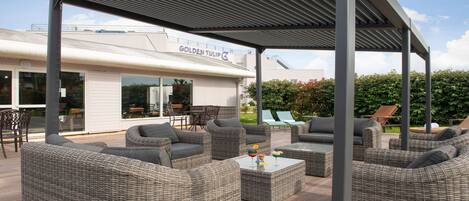 An outdoor patio area with wicker furniture, a covered seating area, and a building labeled "Golden Tulip" in the background.