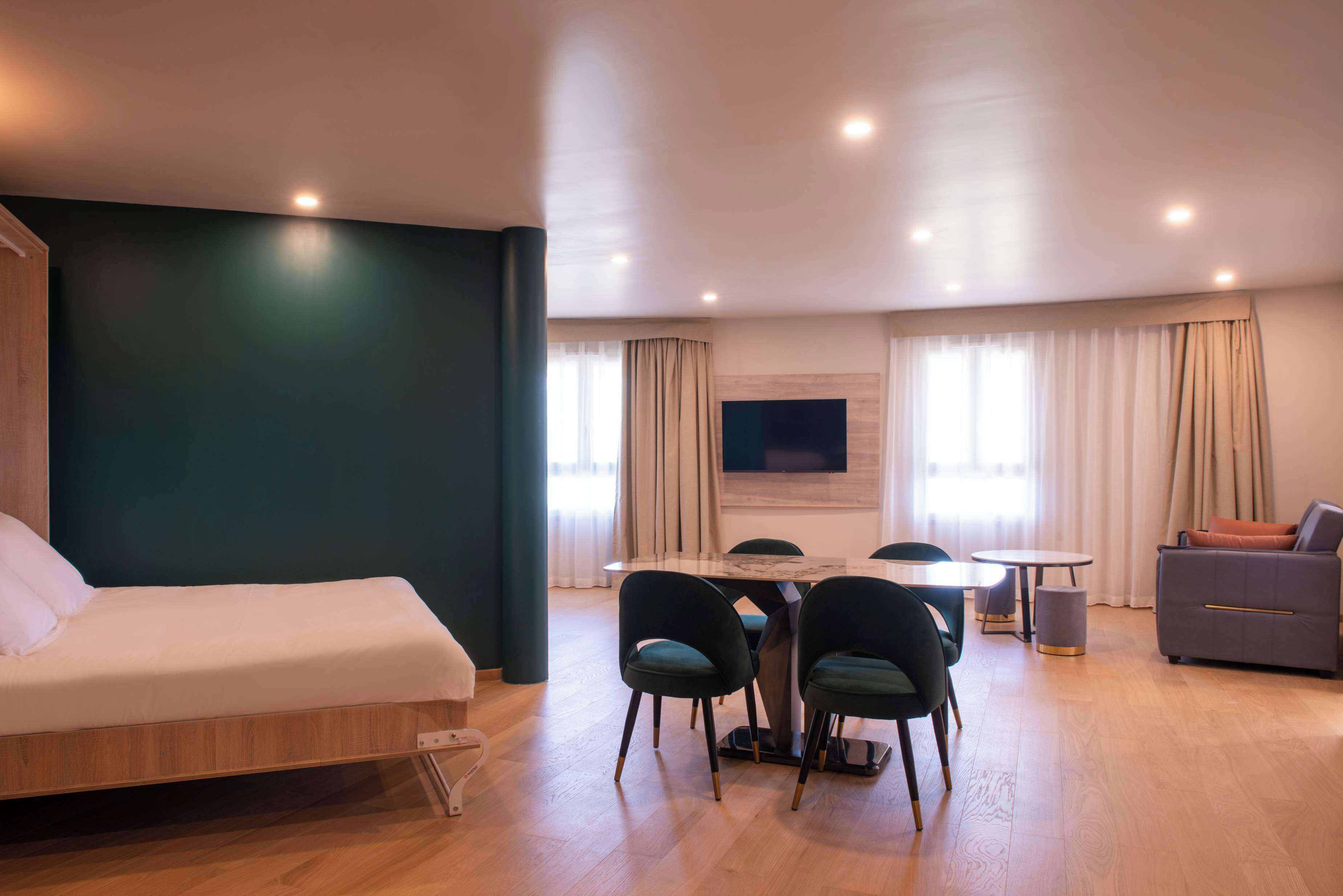 Une chambre d’hôtel moderne équipée d’un lit, d’un coin repas avec des chaises, d’un canapé et d’un téléviseur fixé au mur.