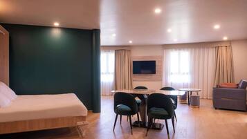 Una camera d'albergo moderna con un letto, un'area pranzo con sedie, un divano e una TV a parete.