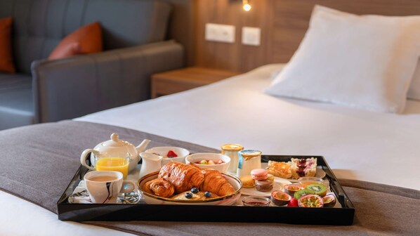 A breakfast tray with croissants, pastries, and fruit on a hotel bed.
