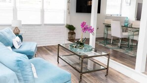 Een woonkamer met een glazen salontafel, een blauwe bank en een eethoek met glazen meubels.