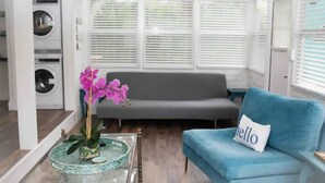 Een woonkamer met een blauwe bank, een glazen salontafel met een roze orchidee, en een wasmachine op de achtergrond.