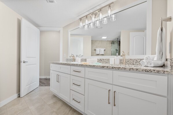 A modern bathroom with a large mirror, white cabinetry, and a marble countertop.