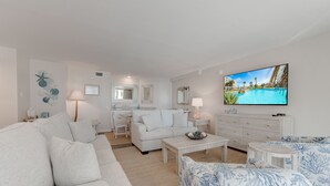 En moderne stue med en hvid sofa, et sofabord og et fjernsyn, der viser udsigt over en pool.