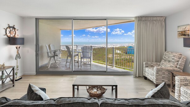 A spacious living room with a large sliding glass door leading to a balcony with a city view. - Sandcastle Condominiums Unit 513 (Port Aransas)