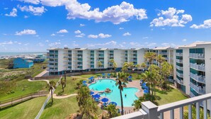 A hotel with a pool area surrounded by palm trees and blue umbrellas, overlooking a beach. - Sandcastle Condominiums Unit 513 (Port Aransas)