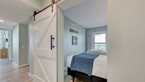 A bedroom with a bed, a sliding door, a window, and a sign on the wall. - Sandcastle Condominiums Unit 523 (Port Aransas)