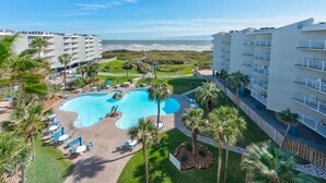 A resort with a large pool, palm trees, and ocean views. - Sandcastle Condominiums Unit 523 (Port Aransas)