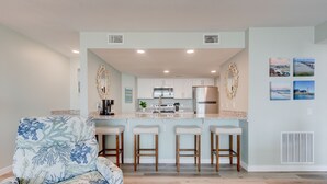 A modern kitchen with white cabinets, stainless steel appliances, and a central island with bar stools. - Sandcastle Condominiums Unit 523 (Port Aransas)