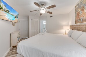 A bedroom with a bed, a ceiling fan, a painting, a nightstand, and a door. - Sandcastle Condominiums Unit 43335 (Port Aransas)